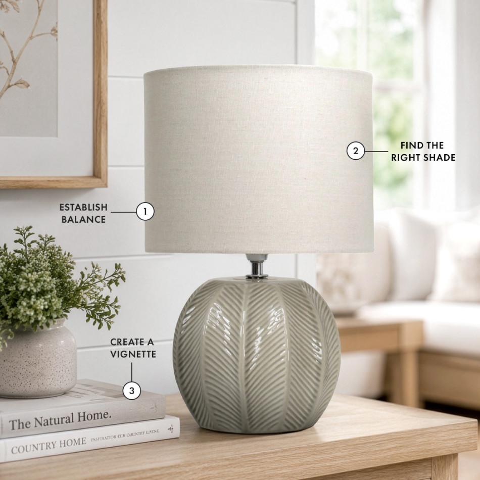 Sage green ceramic table lamp with textured leaf detailing and a linen shade, styled on a timber console with books and greenery, illustrating balanced proportions, thoughtful shade selection and creating a beautifully layered vignette.