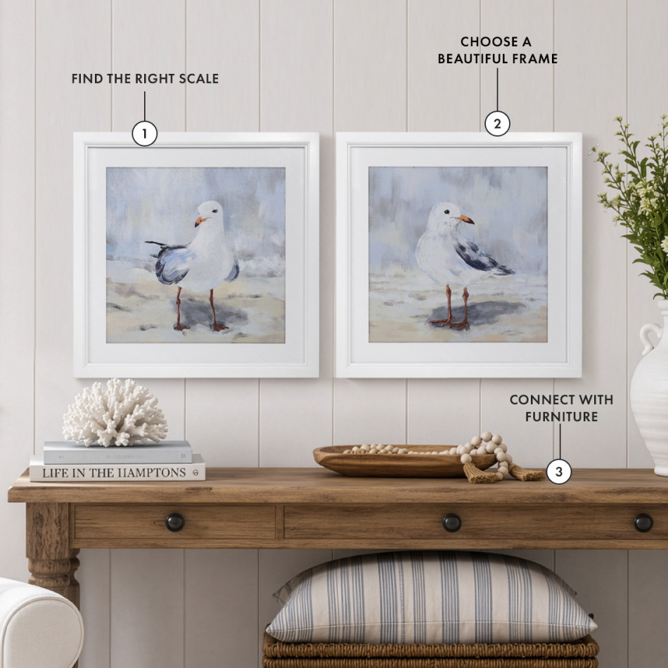 Coastal living room styled with two framed seabird prints above a timber console, illustrating balanced artwork proportions, thoughtful placement and a cohesive blue and neutral colour palette.