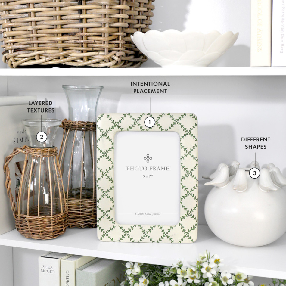 Styled white shelves with a patterned frame, woven glass vessels and sculptural ceramics, illustrating how layered textures, different shapes and thoughtful placement bring depth and interest to a display.