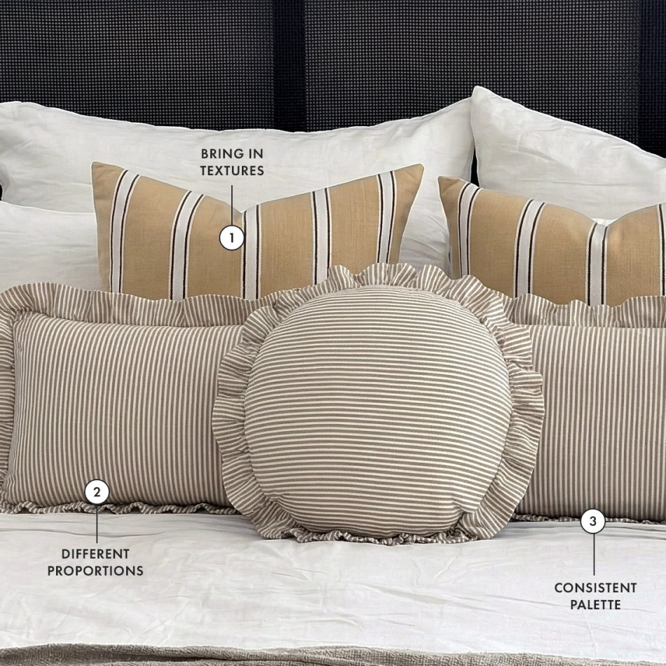 Neutral bed styled with striped cushions in varied sizes and textures, showing how a tonal palette, mixed patterns and layered textures create a balanced, collected look.