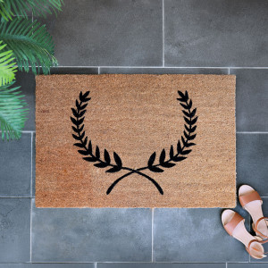 Natural coir entrance mat showing the black laurel wreath design and textured surface