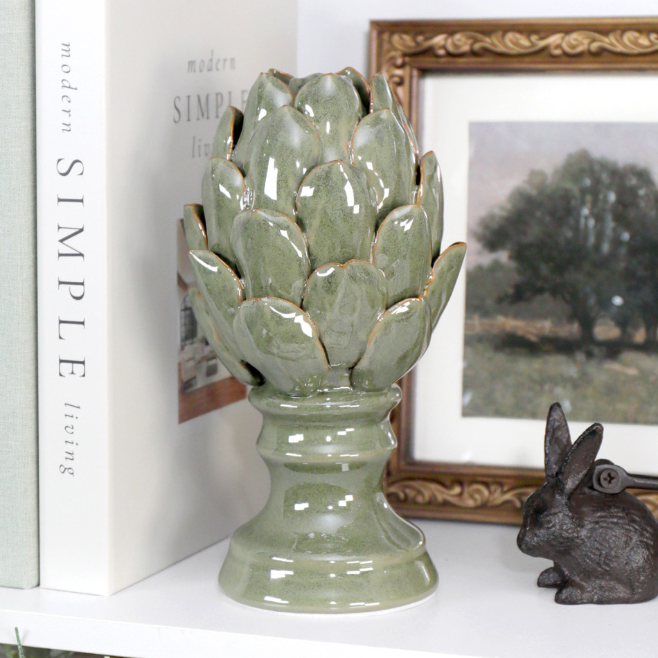 Tall sage green ceramic artichoke ornament styled on a shelf with books and framed artwork