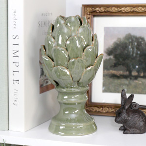 Tall sage green ceramic artichoke ornament styled on a shelf with books and framed artwork