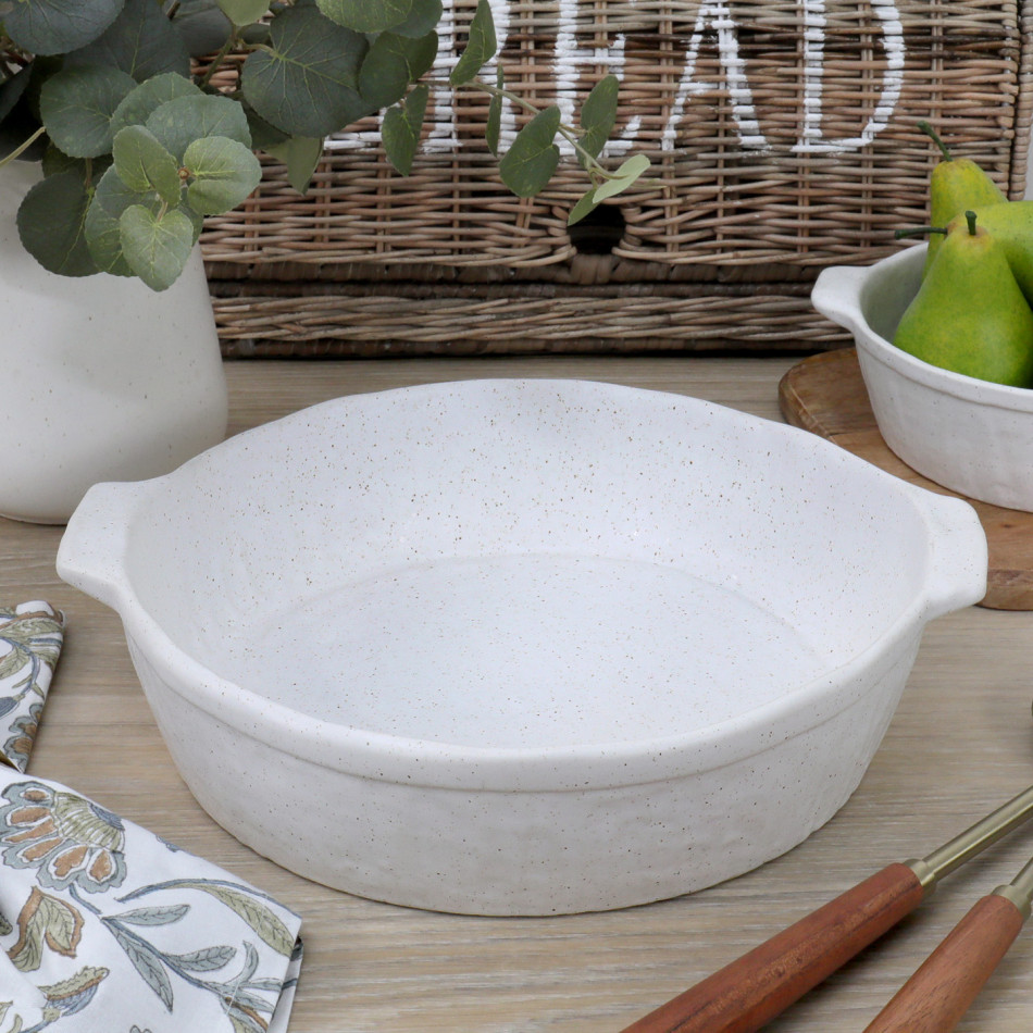 Large round off-white reactive-glaze ceramic baking dish with side handles styled on a kitchen bench