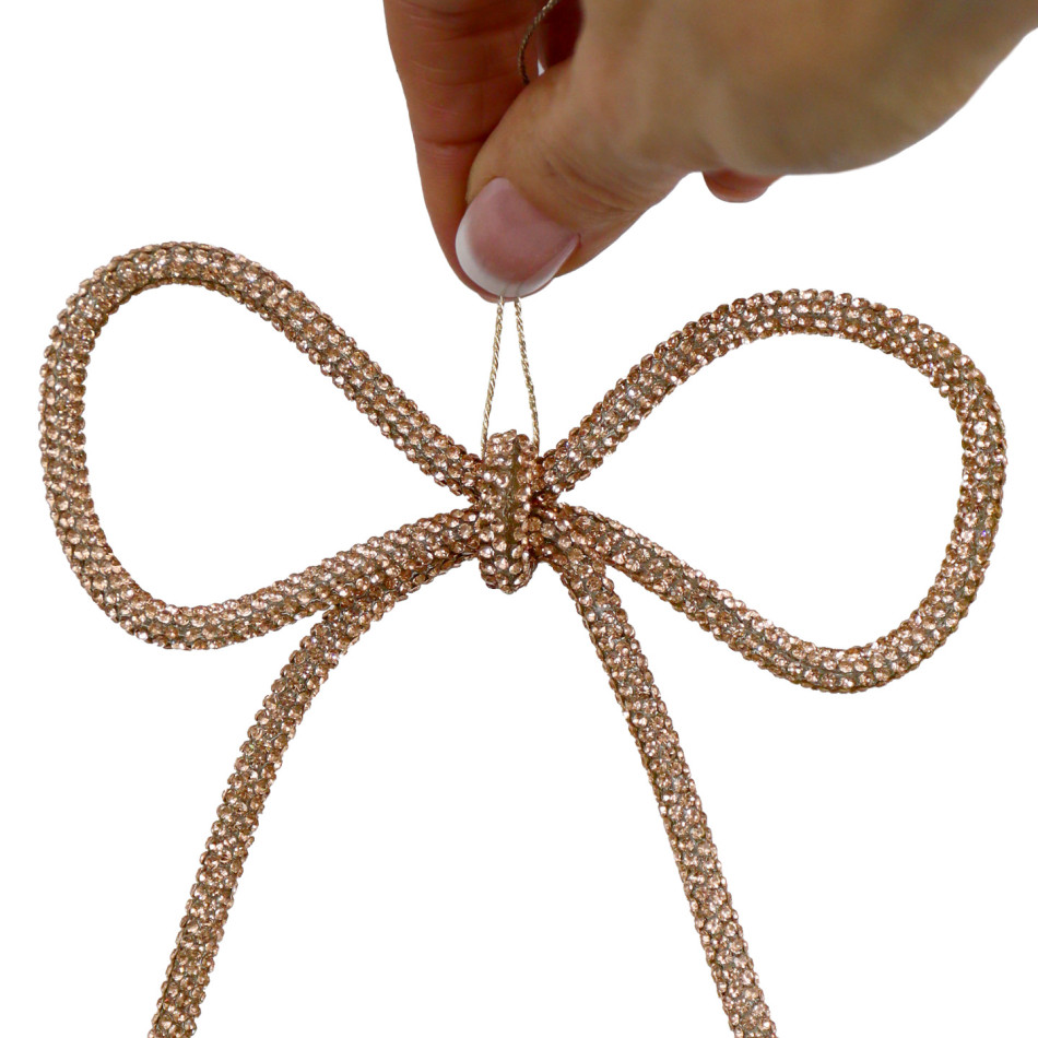 Close-up of a champagne gold diamante bow decoration held by its hanging rope against a white background