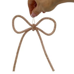 Champagne gold metal bow decoration held by its rope against a white background