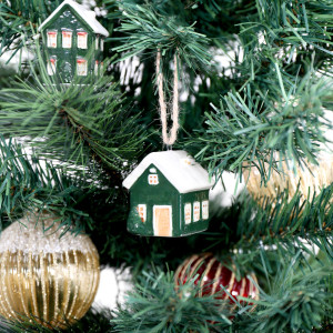 Green bungalow bauble hanging on a Christmas tree with a coordinating green house and gold and red ornaments