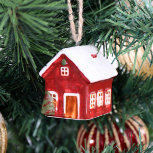 Close-up of red ceramic bungalow tree bauble with a snowy white roof and green tree beside the door