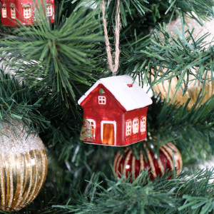 Red ceramic bungalow bauble hanging among Christmas tree branches with gold baubles and another village house