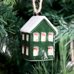 Close-up of handpainted green ceramic house bauble showing pale windows, red accents and a small tree detail