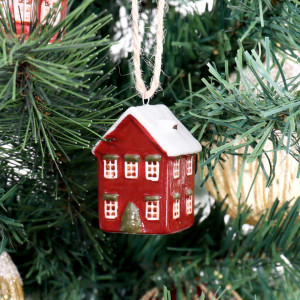 Close-up of red ceramic house bauble with a snowy white roof, white windows and green accents on a Christmas tree