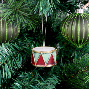Little Drummer Christmas ornament hanging among green branches beside glitter-striped green baubles