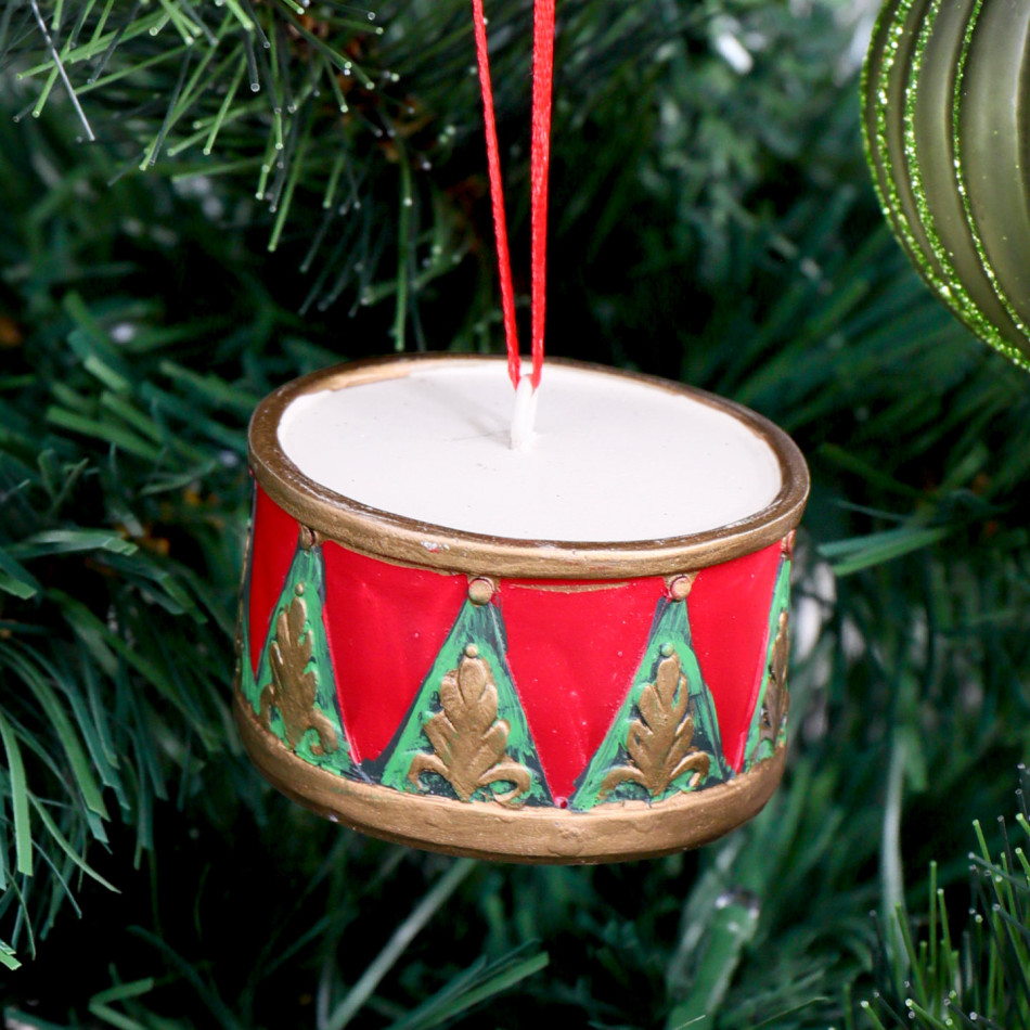 Red and green drum Christmas ornament with gold detailing hanging among tree branches and green baubles