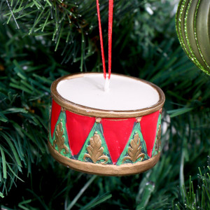 Red and green drum Christmas ornament with gold detailing hanging among tree branches and green baubles