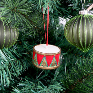 Royal Drummer Christmas ornament hanging from a red ribbon between green striped baubles on a Christmas tree
