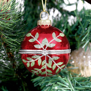 Close-up of Rosalie red glass bauble hanging on a tree, showing its leafy design and decorative metal band
