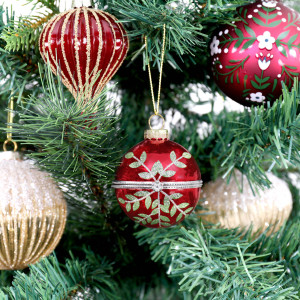 Rosalie round red bauble hanging among red and gold Christmas ornaments on green branches