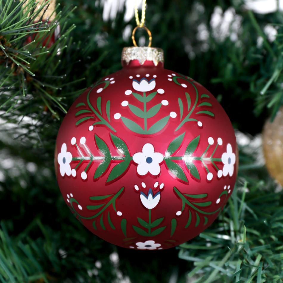 Red Folklore glass bauble hanging on a Christmas tree amongst red and gold ornaments