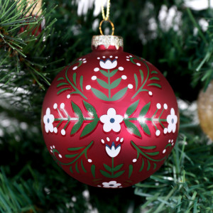 Red Folklore glass bauble hanging on a Christmas tree amongst red and gold ornaments