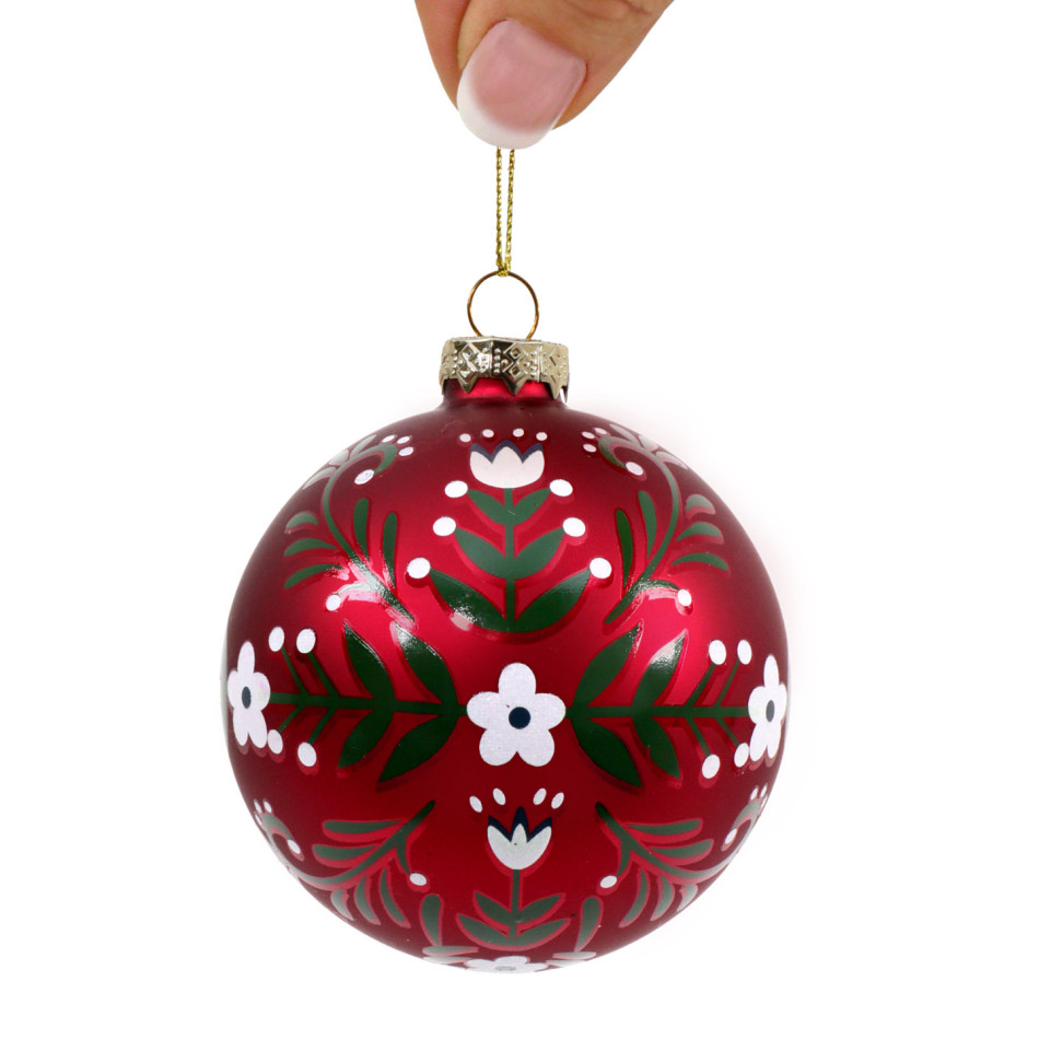 Red floral glass Christmas bauble held by its gold-coloured cord against a white background