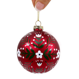 Red floral glass Christmas bauble held by its gold-coloured cord against a white background