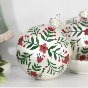 White floral glass Christmas bauble with red glitter detailing and gold-coloured cord on a white surface
