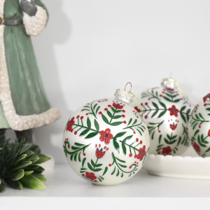 White floral Christmas baubles styled beside a green Santa ornament and festive foliage