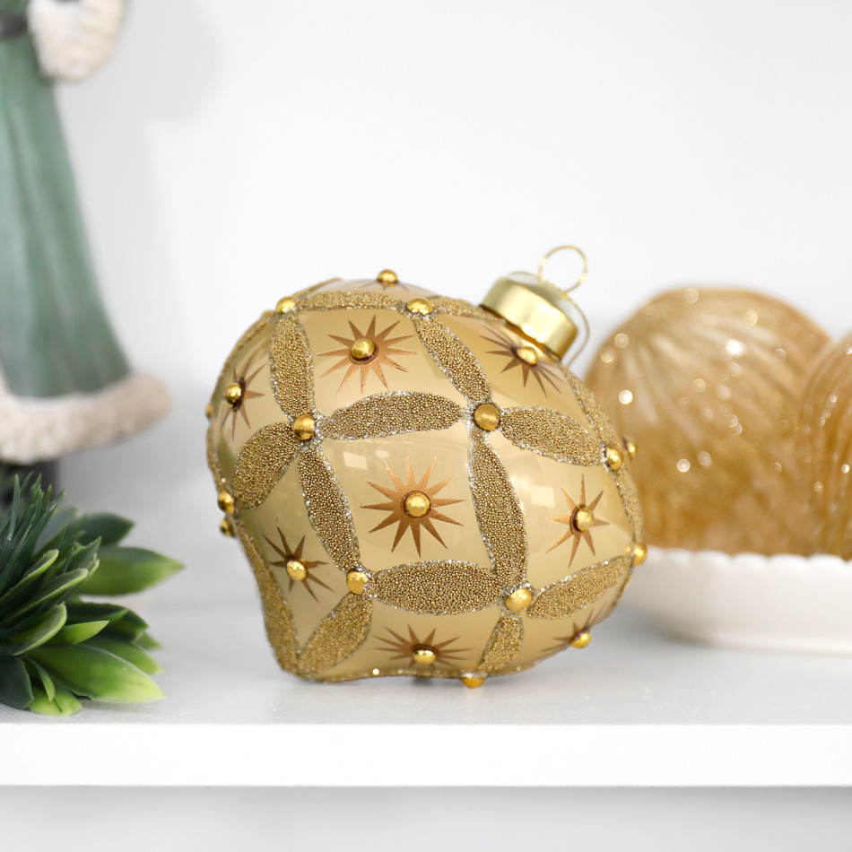 Gold beaded onion decoration resting on a white shelf beside greenery and another gold ornament