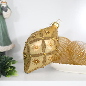 Gold beaded teardrop decoration on a white shelf beside a bowl of gold ornaments and a green Santa figure