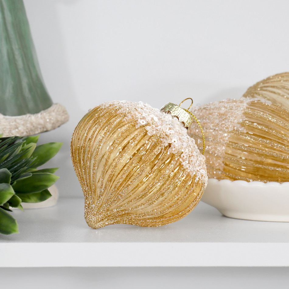 Gold ribbed onion bauble resting on a white shelf beside greenery and a bowl of coordinating ornaments