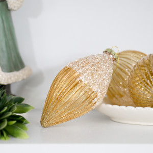 Francesca gold teardrop bauble on a white shelf beside greenery, gold ornaments and a green Santa figure