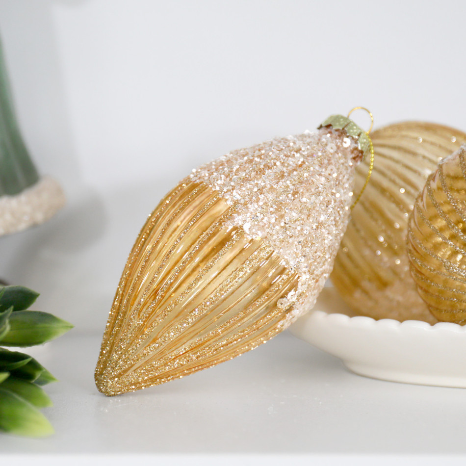 Gold teardrop bauble displayed beside a white bowl of gold ornaments and green foliage