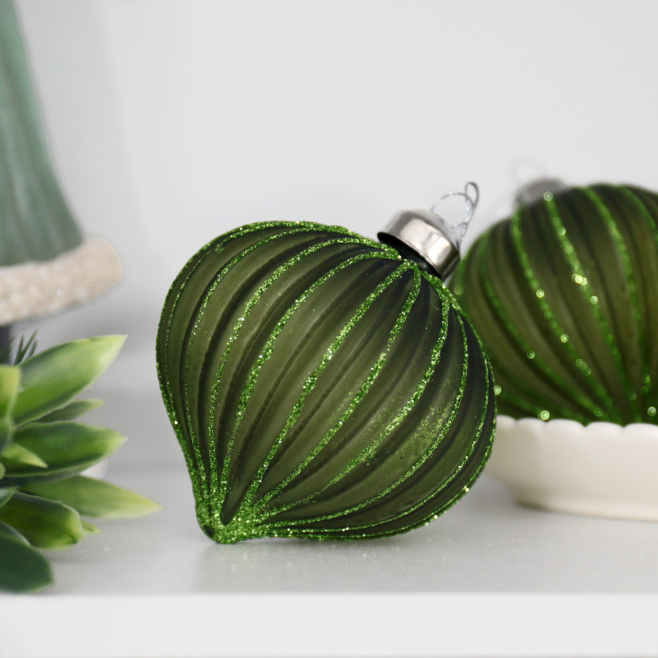 Green glittered onion bauble on a white shelf beside foliage and a bowl of matching green ornaments