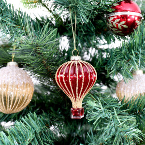 Jules hot air balloon bauble hanging amongst red and gold Christmas ornaments on green branches
