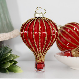 Red and gold glass hot air balloon bauble beside greenery and a white bowl holding another balloon ornament
