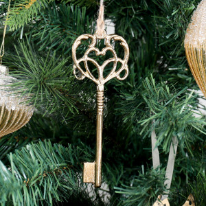 Secret Garden gold key tree decoration with heart-shaped openwork hanging among green Christmas branches.