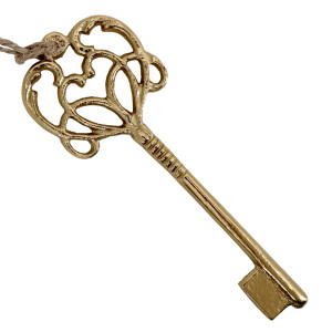 Angled close-up of the gold aluminium key decoration showing scroll detailing and hanging twine on a white background.