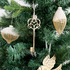 Secret Garden gold key decoration on a Christmas tree beside glittered gold baubles and a gold bird ornament.