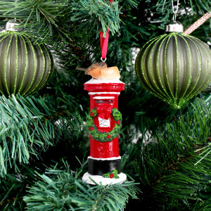 Red pillar box ornament hanging between green glitter baubles on a Christmas tree