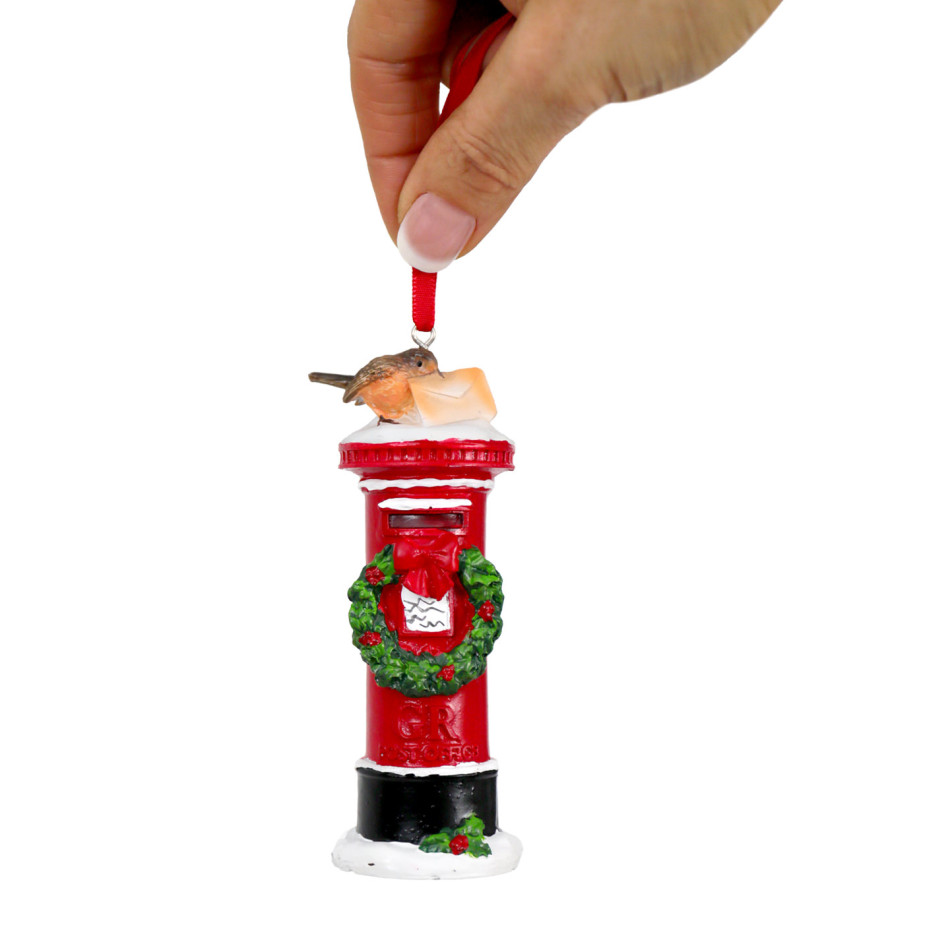 Hand holding a red mailbox Christmas ornament by its ribbon against a white background