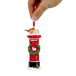 Hand holding a red mailbox Christmas ornament by its ribbon against a white background
