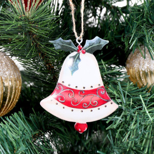Close-up of off-white metal bell decoration with red scrollwork and green holly hanging on a Christmas tree