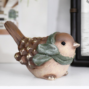 Close-up of Mistletoe Bird wearing a green scarf, with pinecone-inspired wings and gold highlights on a white shelf