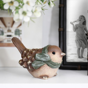 Mistletoe scarf bird displayed on a white shelf beside a dark photo frame and white flowers