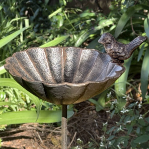 Close-up of Beatty cast iron bird feeder with a scalloped flower dish and decorative bird against garden foliage