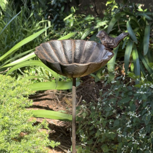 Beatty flower bird feeder on a slender stake in a garden bed surrounded by green foliage