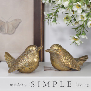 Two antique-style gold bird figurines with detailed feathers styled together on a white book