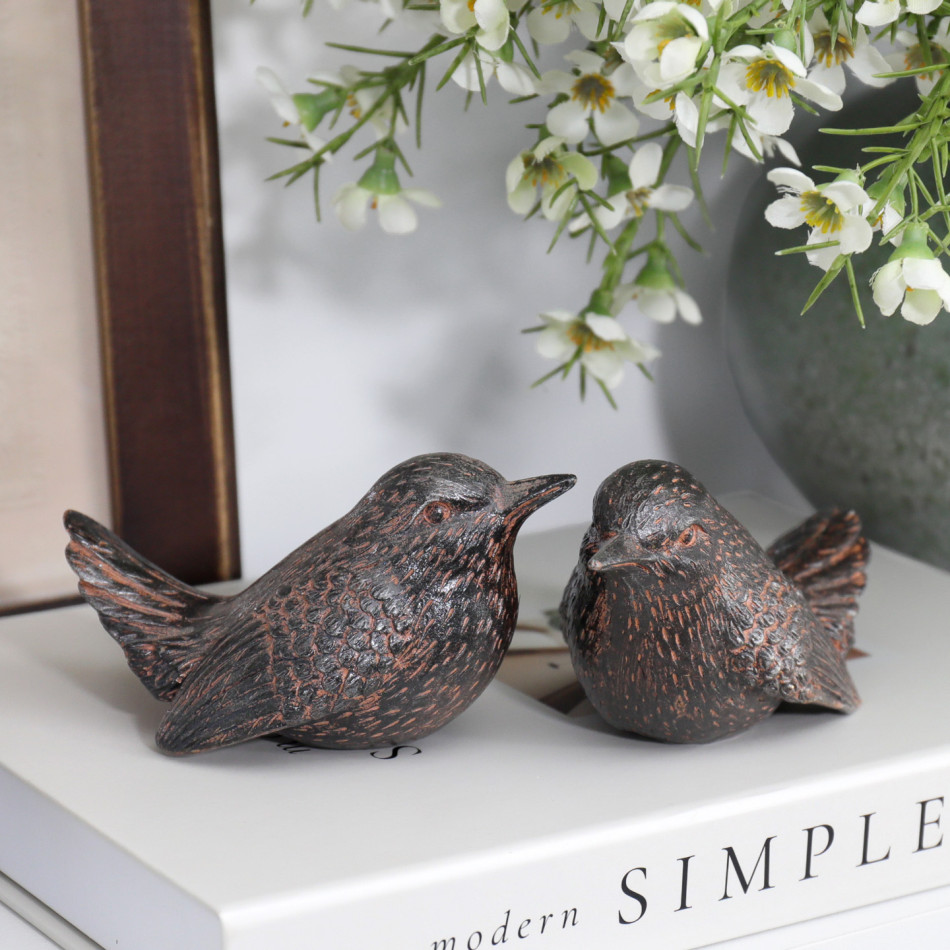 Close view of two textured brown wren ornaments with copper-toned highlights facing each other