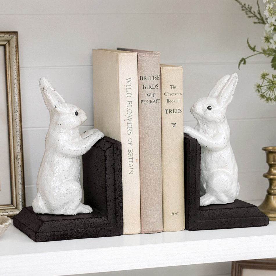 White bunny bookends with dark brown bases holding neutral books on a white country-style shelf