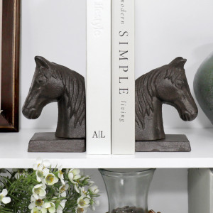 Pair of dark cast iron horse-head bookends supporting books on a styled white shelf